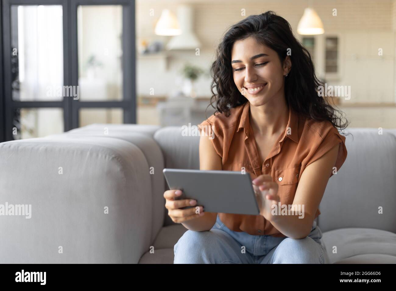 Portrait d'une jeune femme souriante utilisant une tablette, assis sur un canapé à la maison, espace de copie Banque D'Images