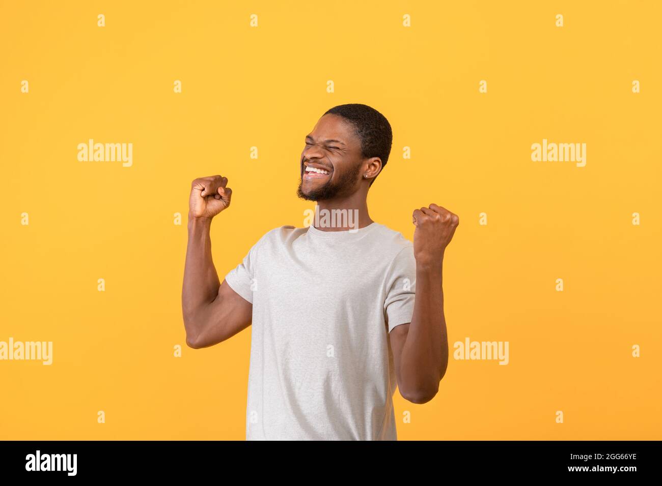 Triomphant homme afro-américain criant dans l'excitation, gestant OUI avec les deux mains sur fond jaune Banque D'Images