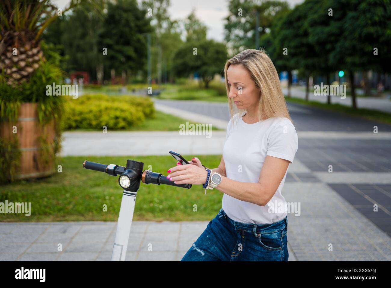 Femme utilisant son smartphone à l'extérieur pour activer par Internet un e-scooter de rue de location. Banque D'Images