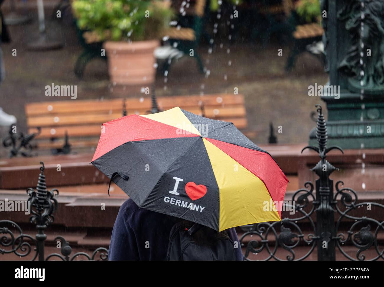 29 août 2021, Hessen, Francfort-sur-le-main: Un homme se tient sur le dimanche des pluies avec un parapluie avec l'inscription "I love Germany" à la fontaine de justice sur le Römerberg. Photo: Frank Rumpenhorst/dpa Banque D'Images