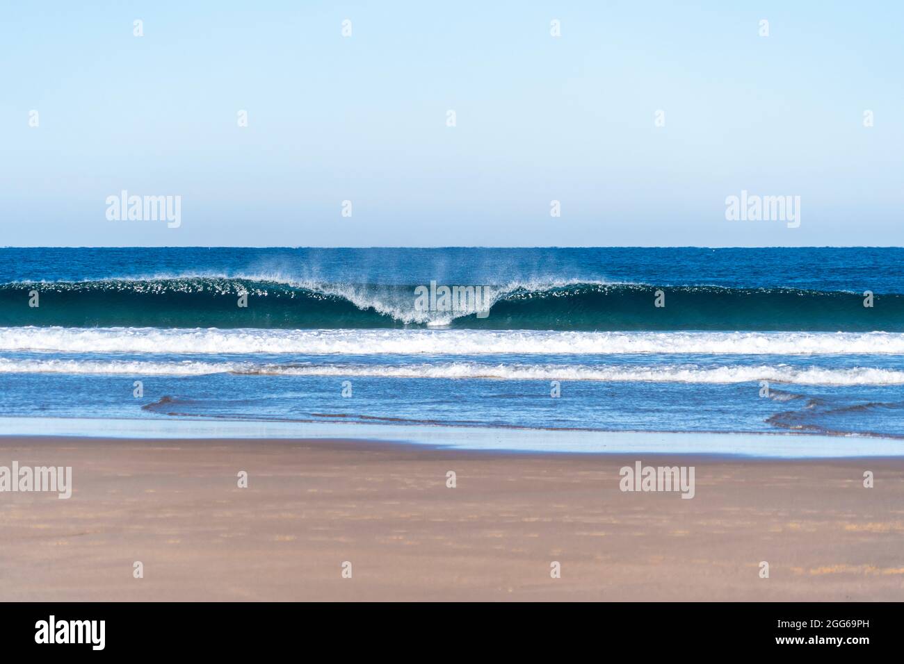 Une vague qui se déferle un matin ensoleillé. Tonneau à vagues parfait avec vent offshore sur une plage de sable Banque D'Images