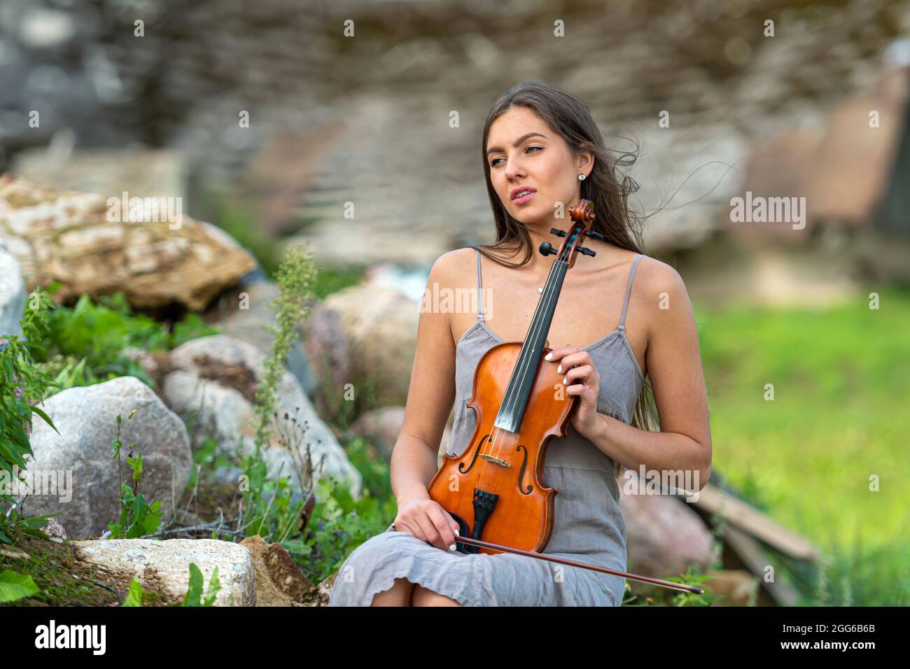 belle brune dans une robe de lin avec un violon sur une pile de rochers dans une ancienne maison de campagne Banque D'Images