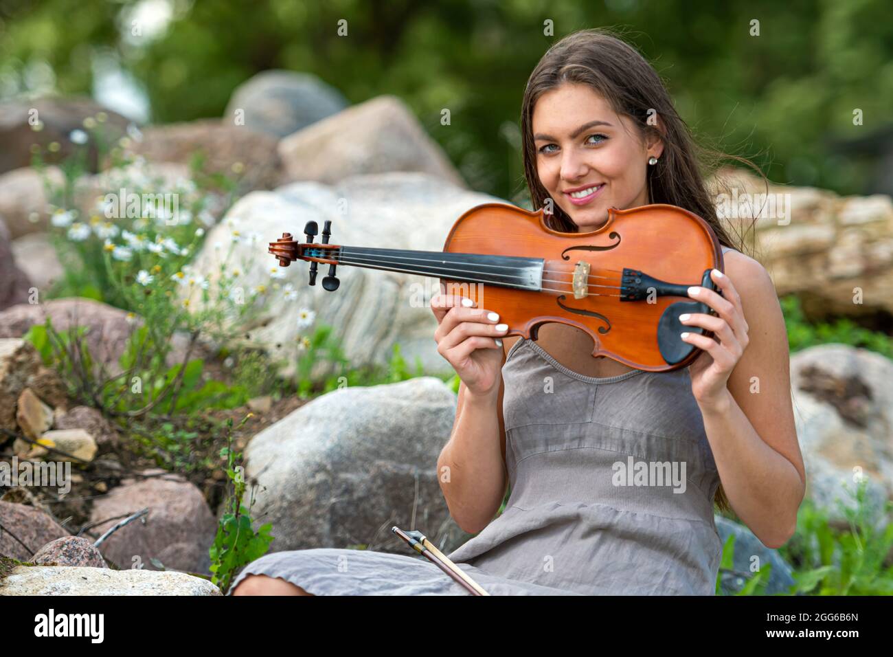 belle brune dans une robe de lin avec un violon sur une pile de rochers dans une ancienne maison de campagne Banque D'Images