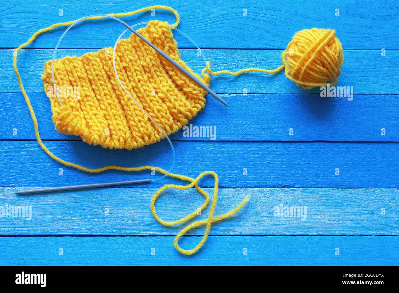 tricoter, passe-temps concept. Tissu tricoté jaune avec aiguilles à tricoter et boule de laine sur table rustique bleue. Copier l'espace Banque D'Images