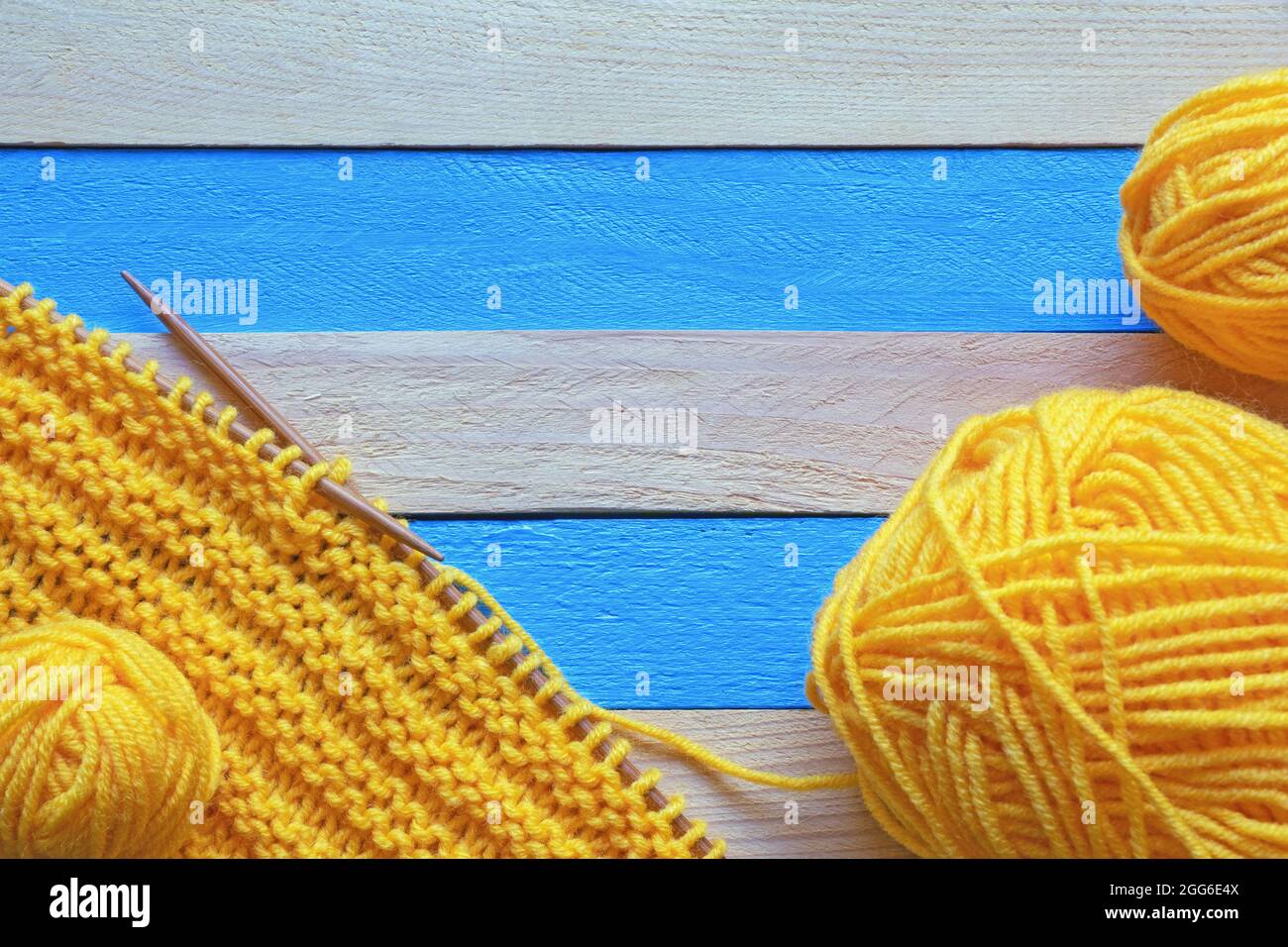 Passe-temps et concept de tricotage. Tissu tricoté avec aiguilles à tricoter et pelins de laine sur table rustique. Espace pour le texte Banque D'Images
