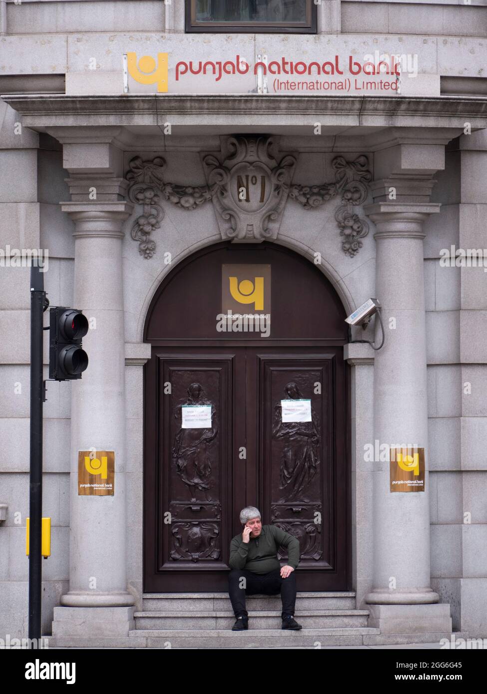 Homme assis sur les marches de la banque nationale du Punjab dans la ville de Londres, Royaume-Uni Banque D'Images