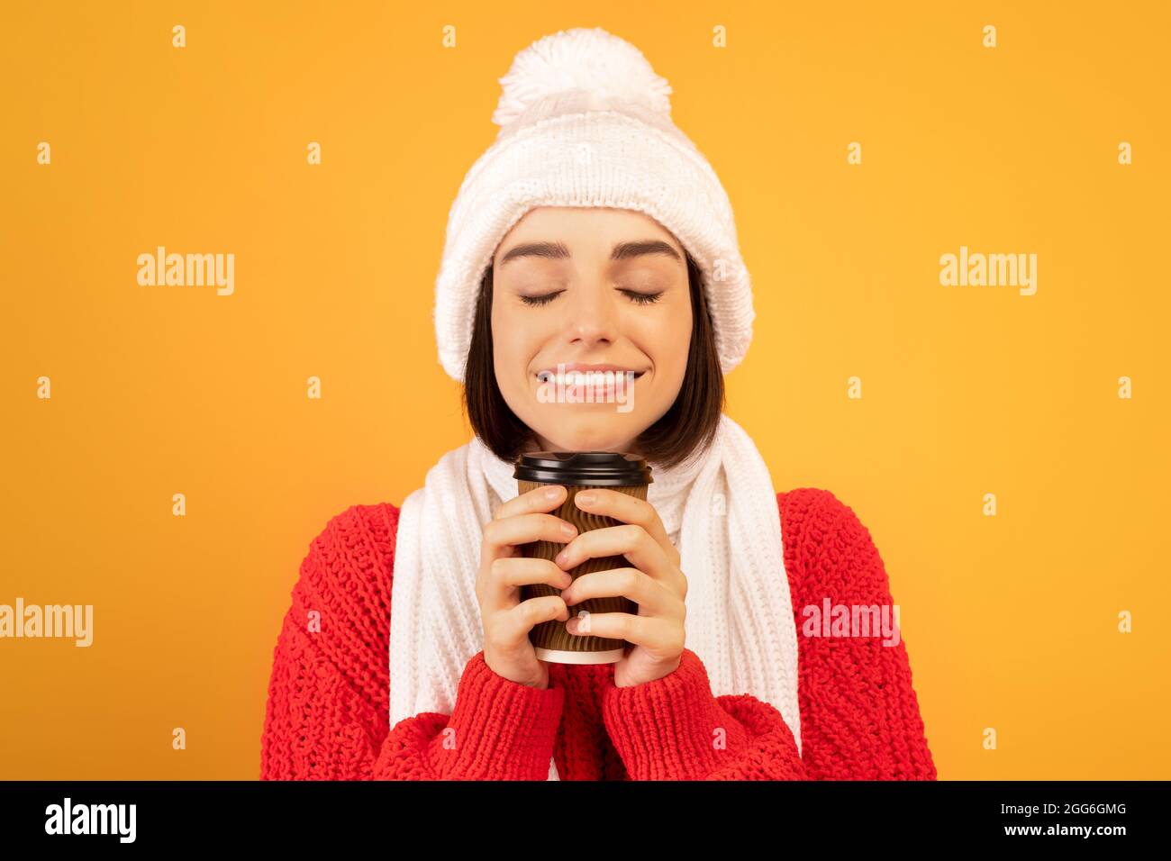 Faites une pause chaude. Jolie dame en chapeau d'hiver et écharpe tenant une tasse de café en papier et appréciant l'odeur aromatique Banque D'Images