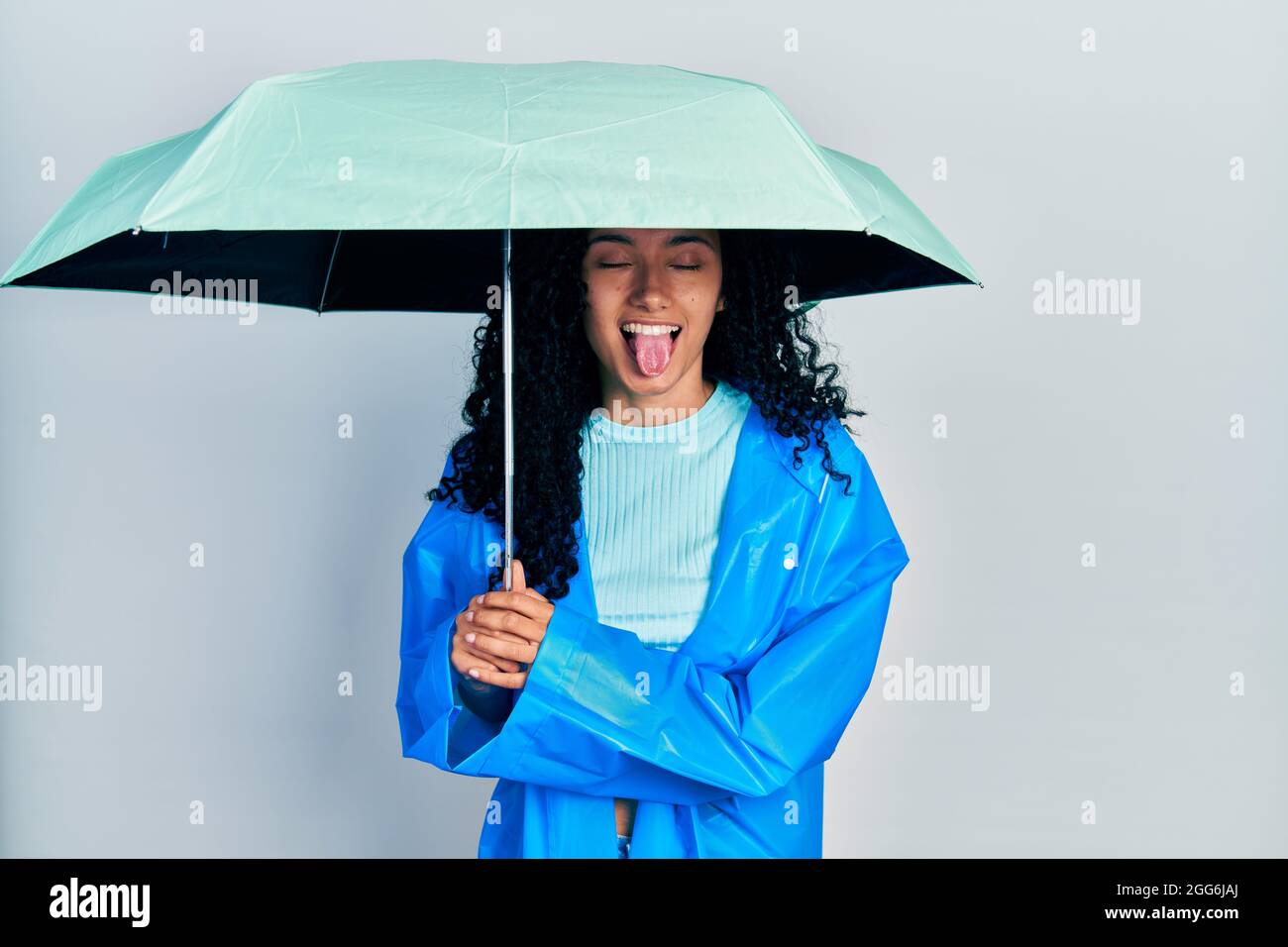 Jeune femme hispanique aux cheveux bouclés portant un imperméable et un  parapluie collant la langue heureux avec l'expression drôle Photo Stock -  Alamy