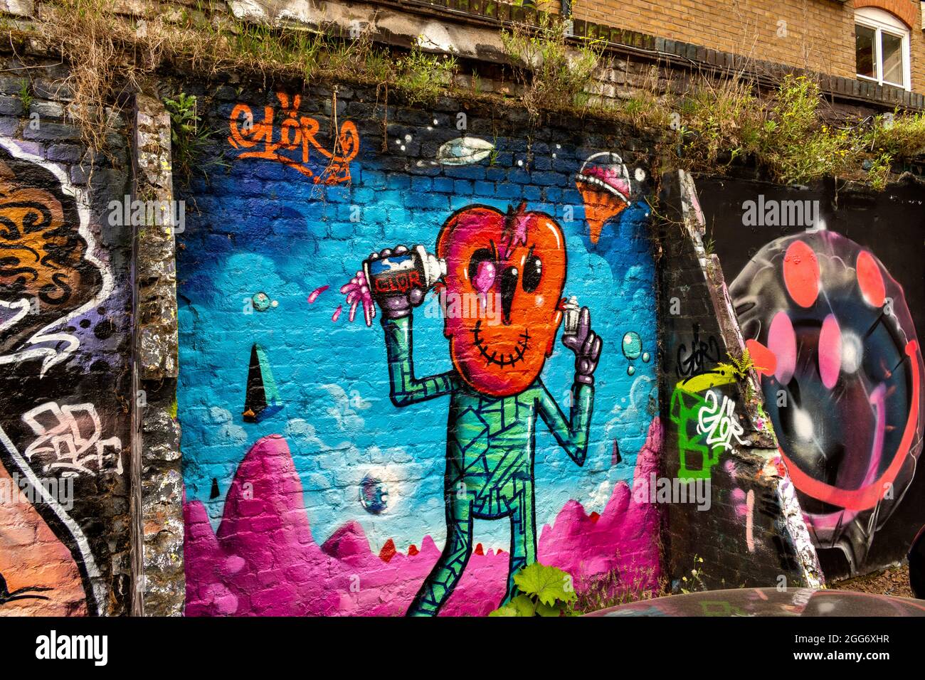 ESPACE ARTISTIQUE ET CULTUREL DE LONDRES AUTOUR DE LA RUELLE DE BRIQUES AVEC DES MOTIFS CRÉATIFS ET DES SLOGANS COLORÉS MUR AVEC HERBE ET FLEURS Banque D'Images