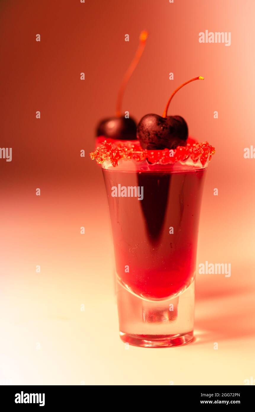 Cocktail rouge rubis à base de vodka, liqueur de cerise et sirop dans un  verre à boisson, décoré avec de la cerise fraîche et du sucre rouge,  boisson sucrée Photo Stock -