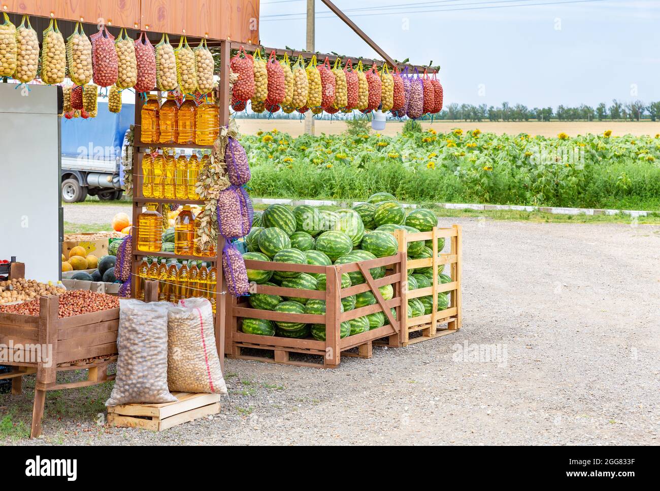 Les agriculteurs de bord de route vendent des produits bio sur fond de champ avec des tournesols. Huile végétale en bouteilles, pommes de terre en filets Banque D'Images