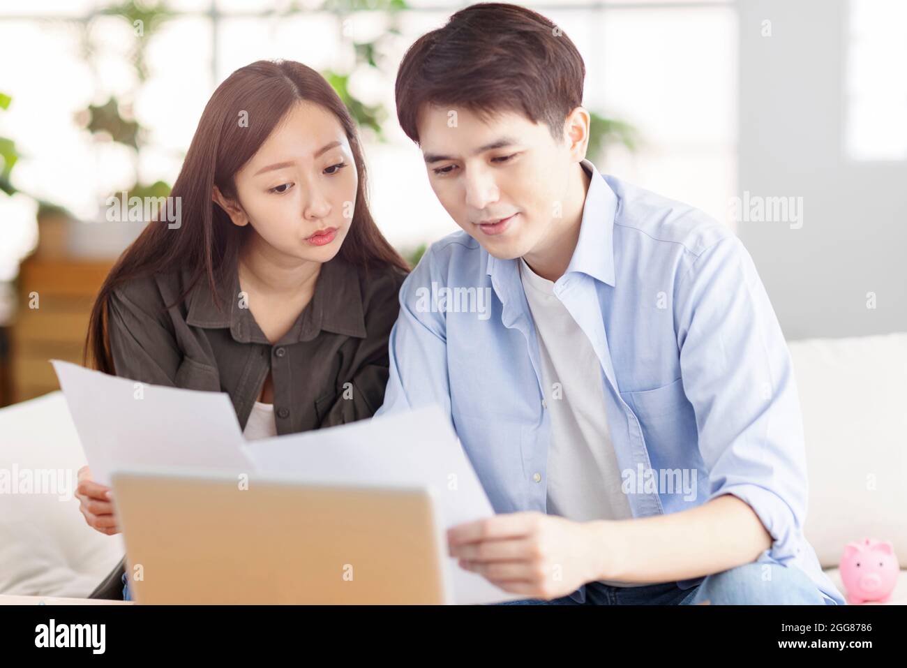 Un jeune mari et une jeune femme qui tient des documents administratifs et qui utilisent un ordinateur portable à la maison. Banque D'Images