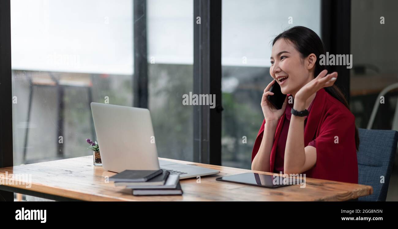 Portrait jeune femme d'affaires asiatique beau charmant souriant et parlant sur le téléphone mobile au bureau. Femme travaillant avec un ordinateur portable Banque D'Images