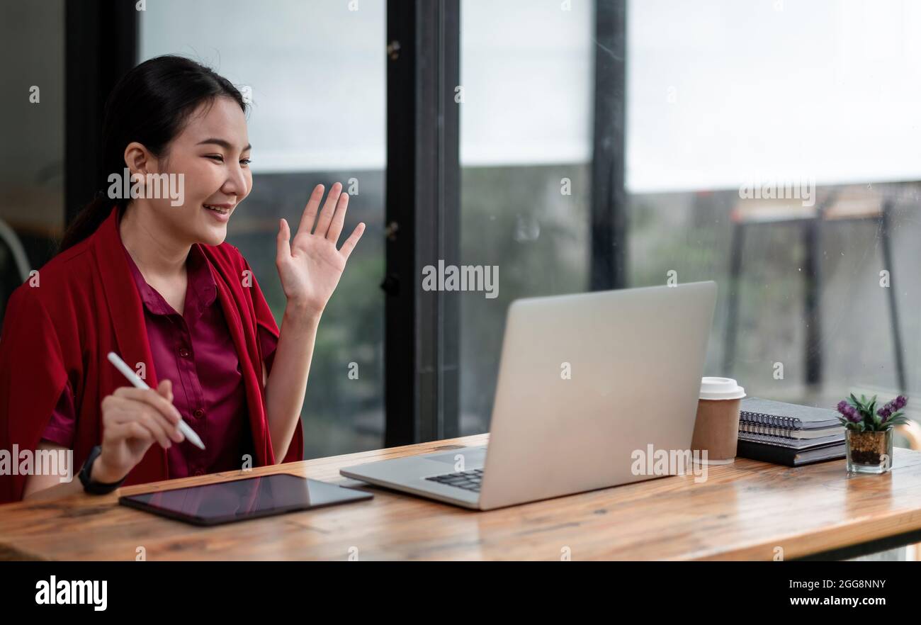 Gros plan photo de positive gaie asiatique fille ont en ligne appel vidéo de diffusion dire hi vague main s'asseoir table utiliser ordinateur portable dans la maison Banque D'Images
