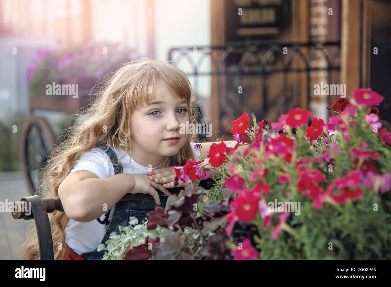 Portrait d'une jeune fille de 11 ans dans la rue avec des fleurs pétunia. Elle sourit et pose au coucher du soleil. Banque D'Images