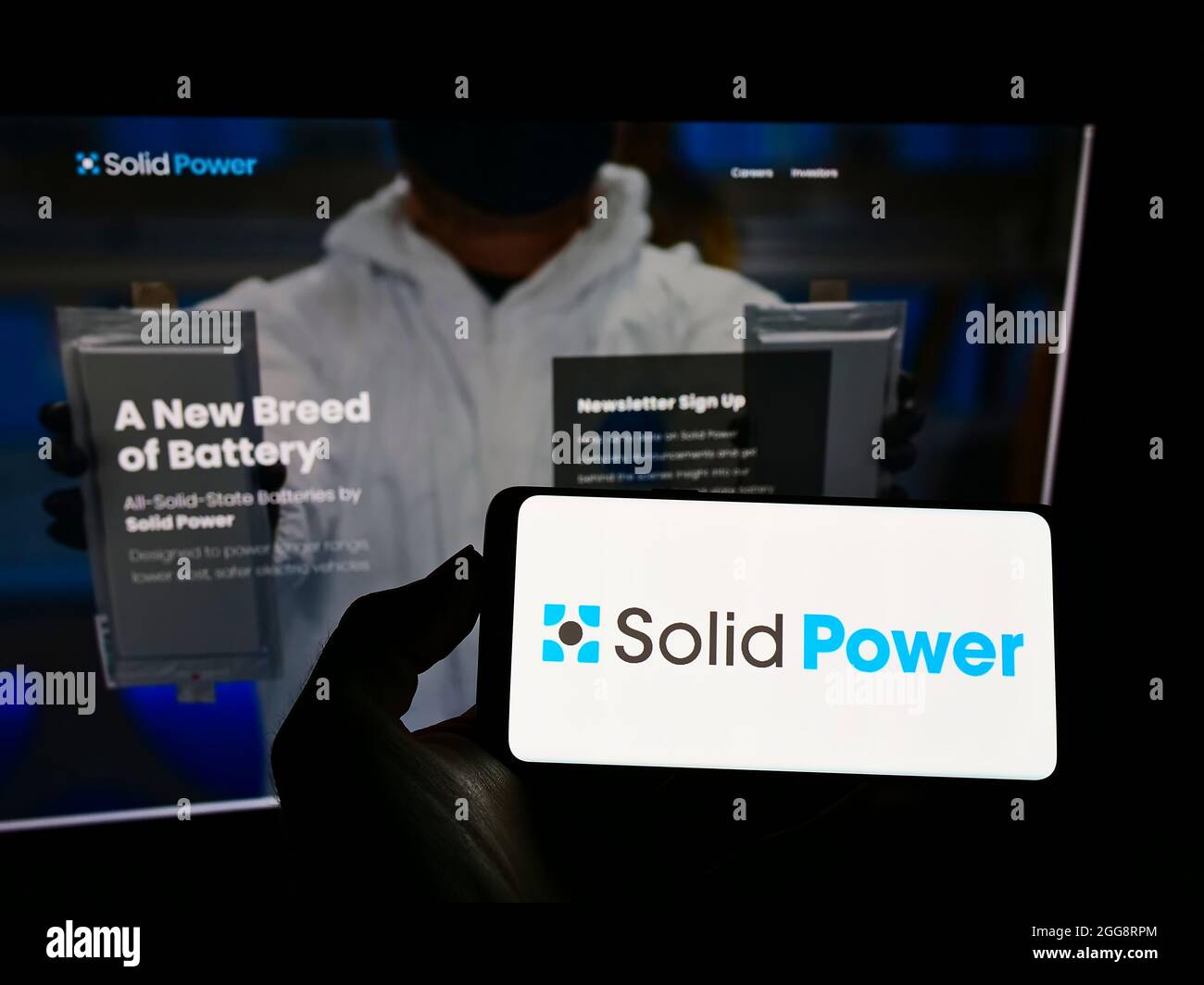 Personne tenant un téléphone portable avec le logo de la société américaine de batterie Solid Power Inc. À l'écran en face de la page Web d'affaires. Mise au point sur l'affichage du téléphone. Banque D'Images