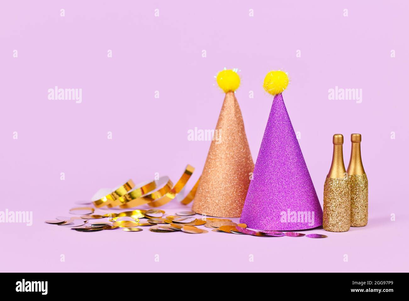 Chapeau de fête étincelant, petites bouteilles de champagne dorées et banderoles de fête sur fond violet avec espace pour les copies Banque D'Images