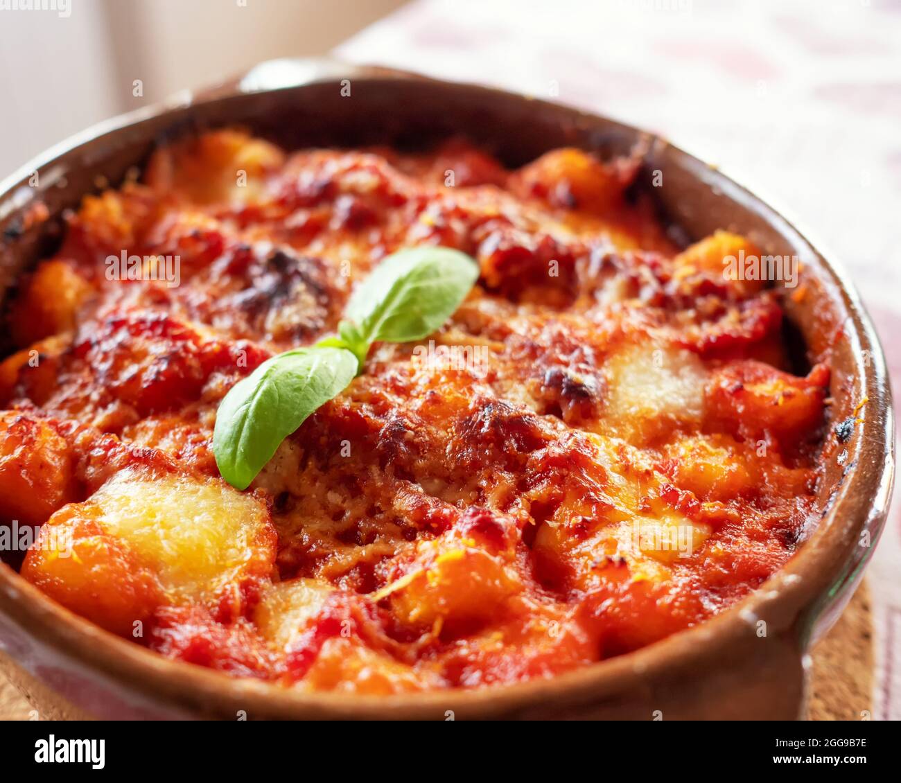 Gnocchi alla Sorrentina, boulettes de pommes de terre italiennes à la sauce tomate, gratinées avec du fromage mozzarella dans un plat en terre cuite. Mise au point sélective. Banque D'Images