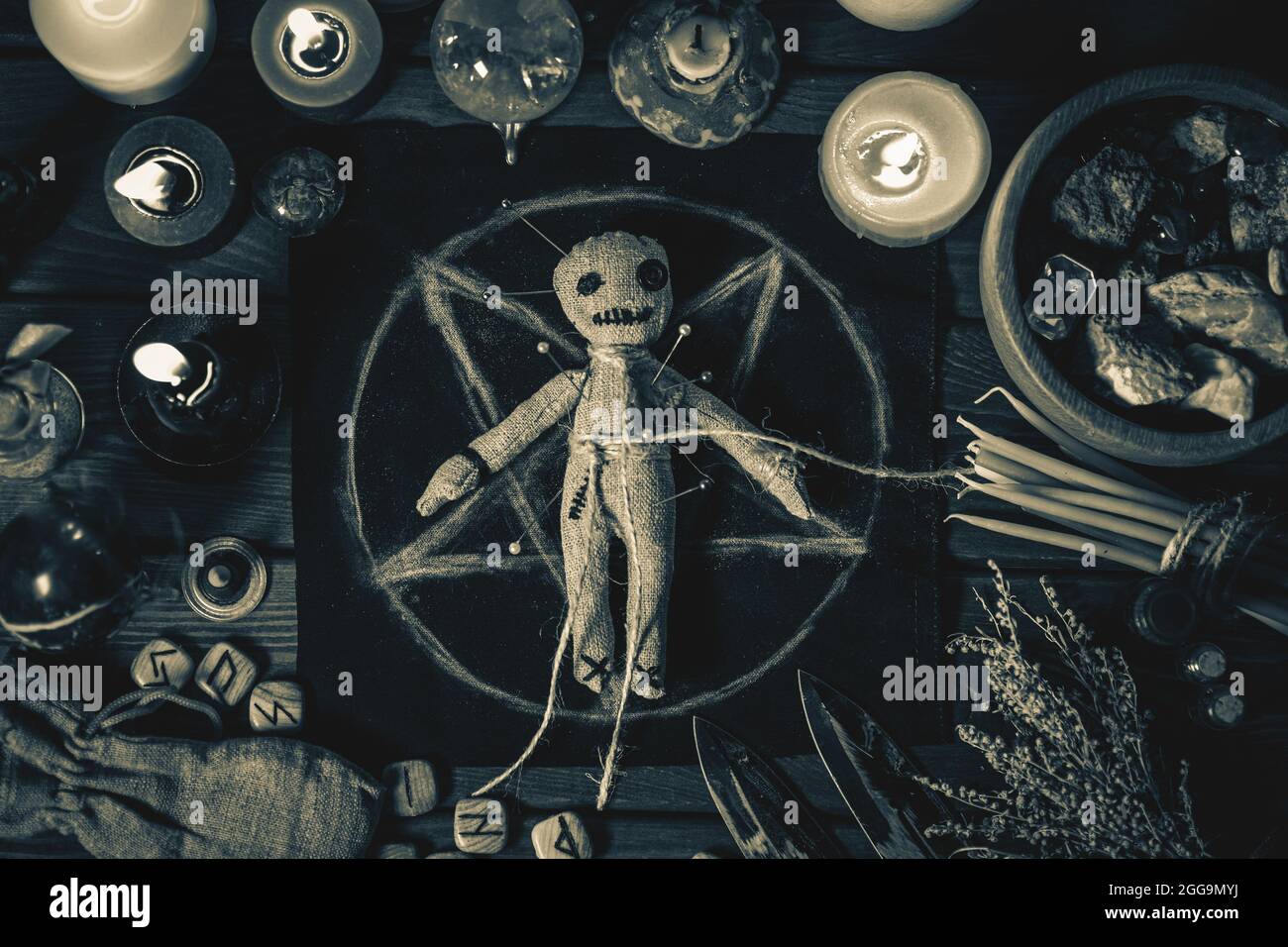 Voodoo Magic concept. Poupée Voodoo clouée avec des aiguilles avec un coeur de chiffon percé sur le pentagramme et autour des bougies en feu. Rituel ésotérique magique effrayant ou inquiétant, photo en noir et blanc. Banque D'Images