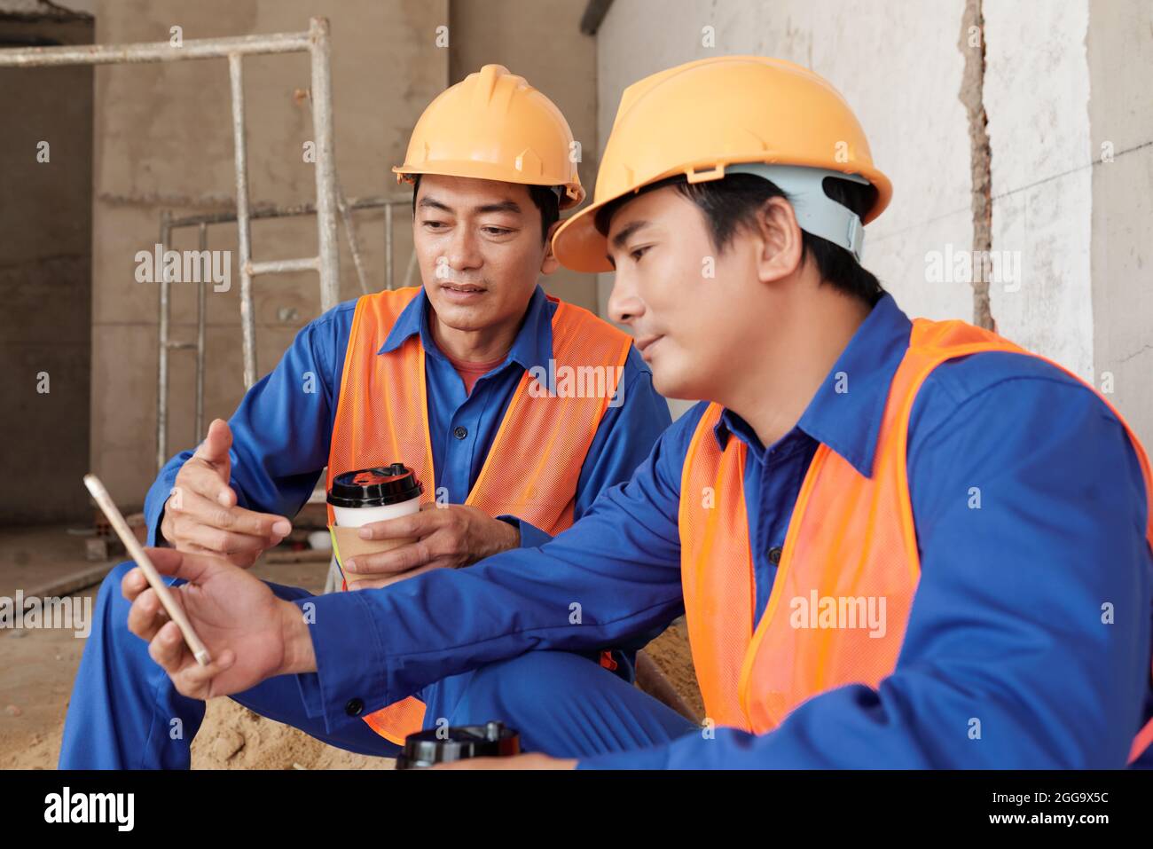 Les ouvriers de la construction en uniforme et en casque de sécurité discutent de nouveaux souvenirs sur les médias sociaux lorsqu'ils font une pause-café Banque D'Images