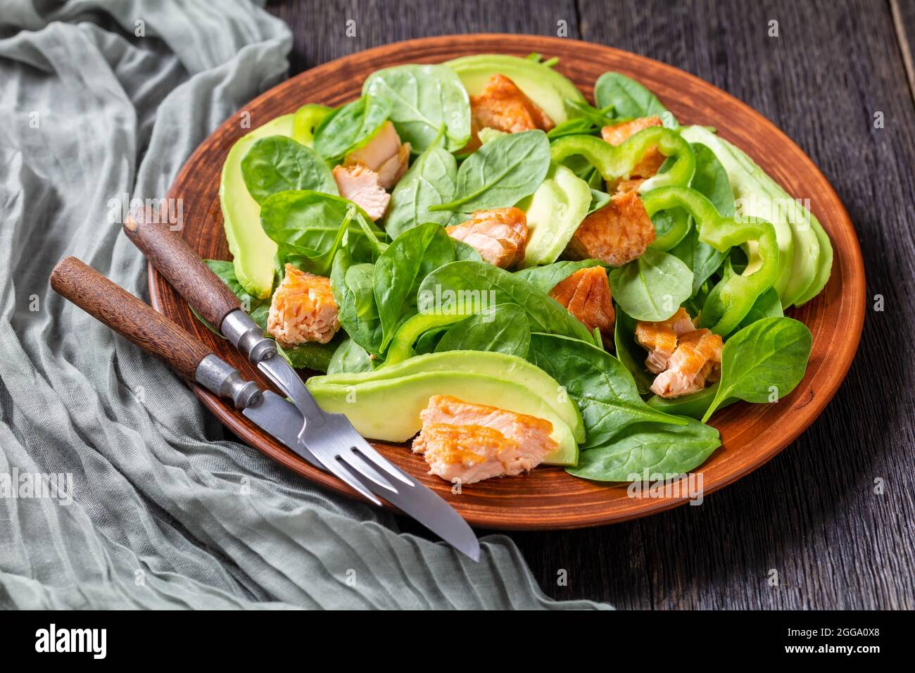 salade de saumon à l'avocat aux épinards et au poivre vert sur une assiette rustique brune avec fourchette et couteau sur une table de bog en chêne, déjeuner méditerranéen Banque D'Images