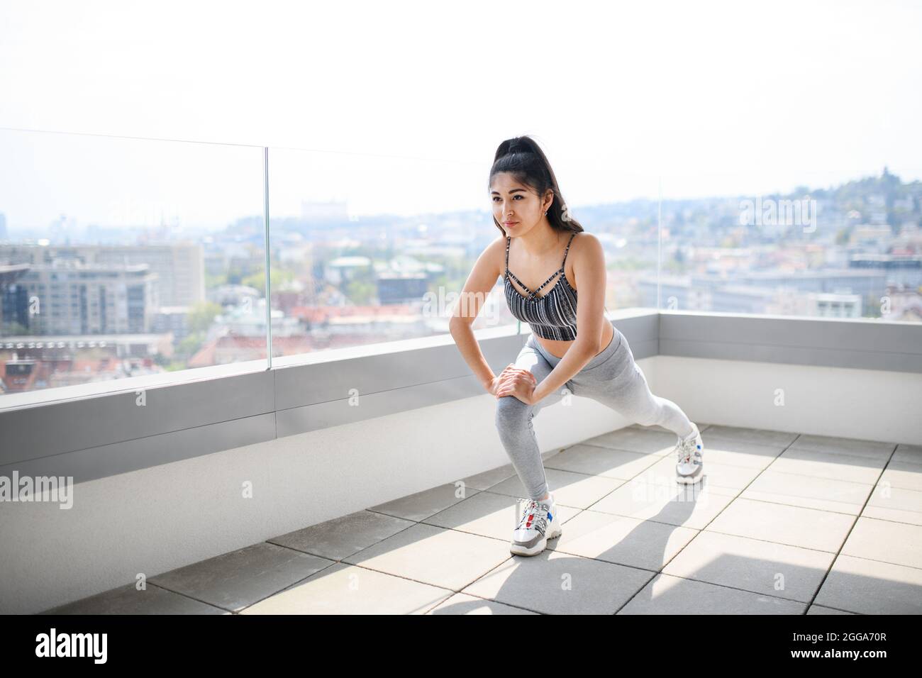 Portrait d'une jeune femme de sport faisant de l'exercice sur un balcon à l'extérieur de la ville, s'étirant. Banque D'Images