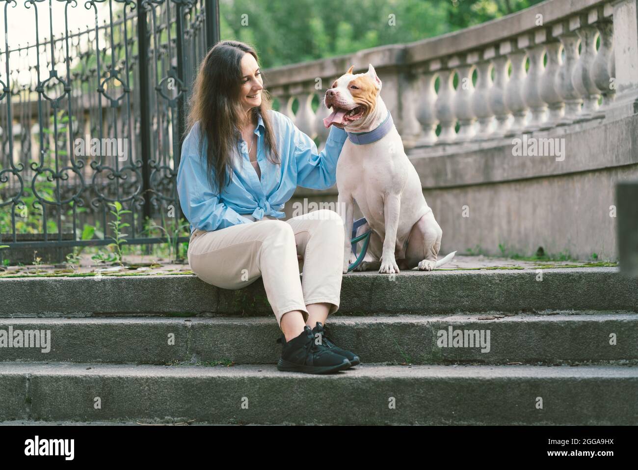 Femme assise sur un escalier en pierre et patting de pitbull américain terrier. Chien heureux regardant le propriétaire Banque D'Images