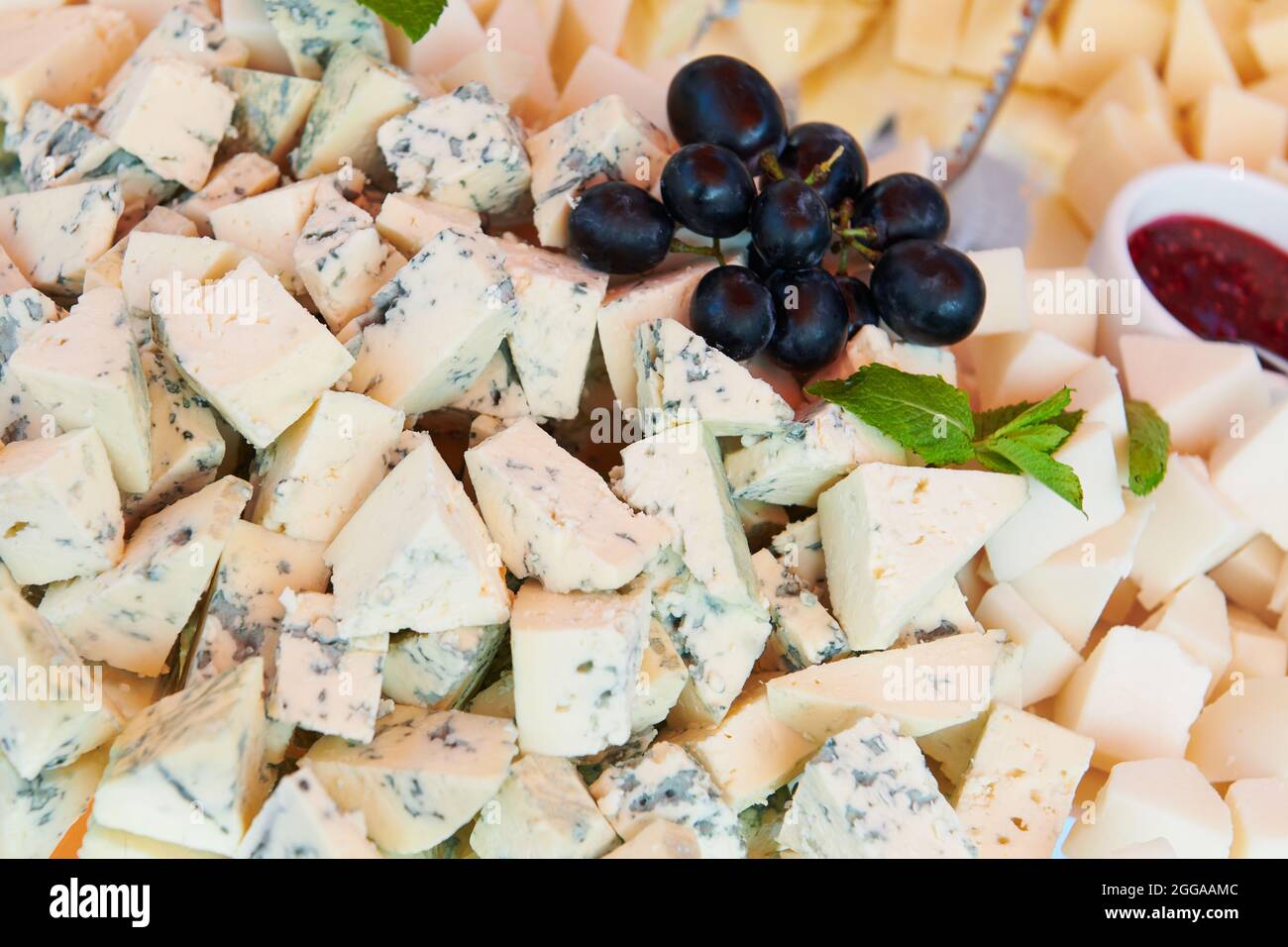 Assiette de fromages avec confiture de framboises décorée de menthe et de raisin bleu. Fromage bleu et fromage de chèvre. Restauration de luxe. Gros plan. Banque D'Images