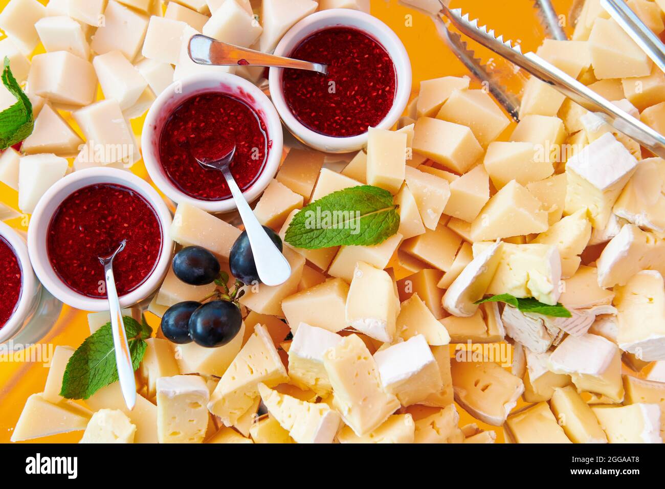 Assiette de fromages avec confiture de framboises décorée de menthe et de raisin bleu. Brie et fromage de chèvre. Restauration de luxe. Vue de dessus. La nourriture. Banque D'Images