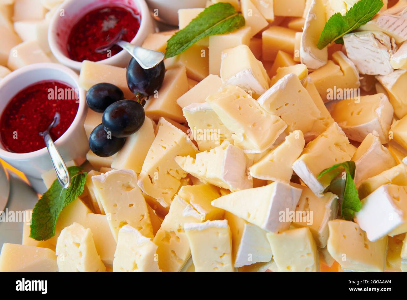 Assiette de fromages avec confiture de framboises décorée de menthe et de raisin bleu. Brie et fromage de chèvre. Restauration de luxe. Gros plan. Banque D'Images