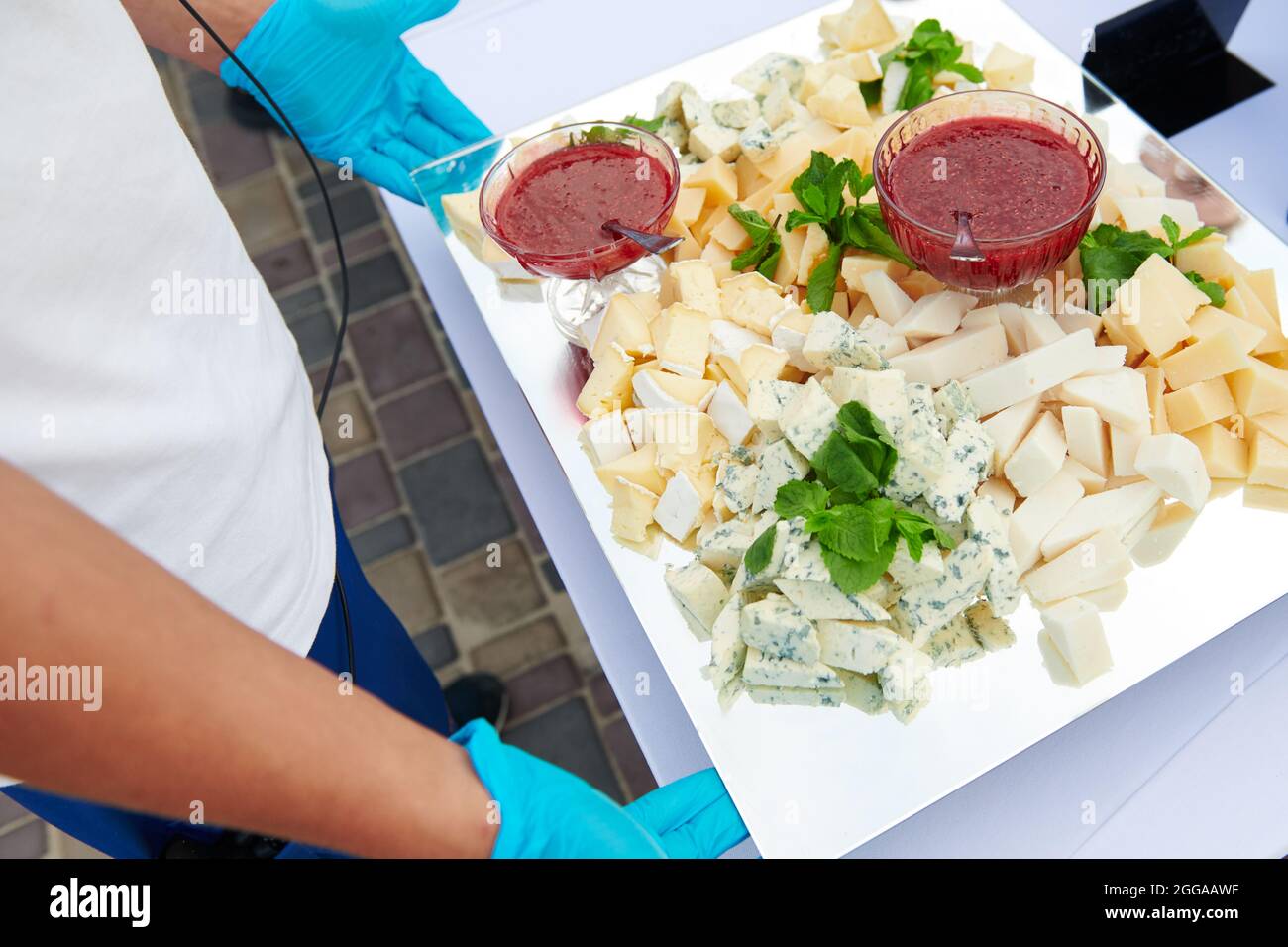 Garçon en gants bleus servant une assiette de fromage à l'événement. Différents types de fromage servis avec de la confiture de framboise décorée de menthe. Fromage bleu et brie. Banque D'Images