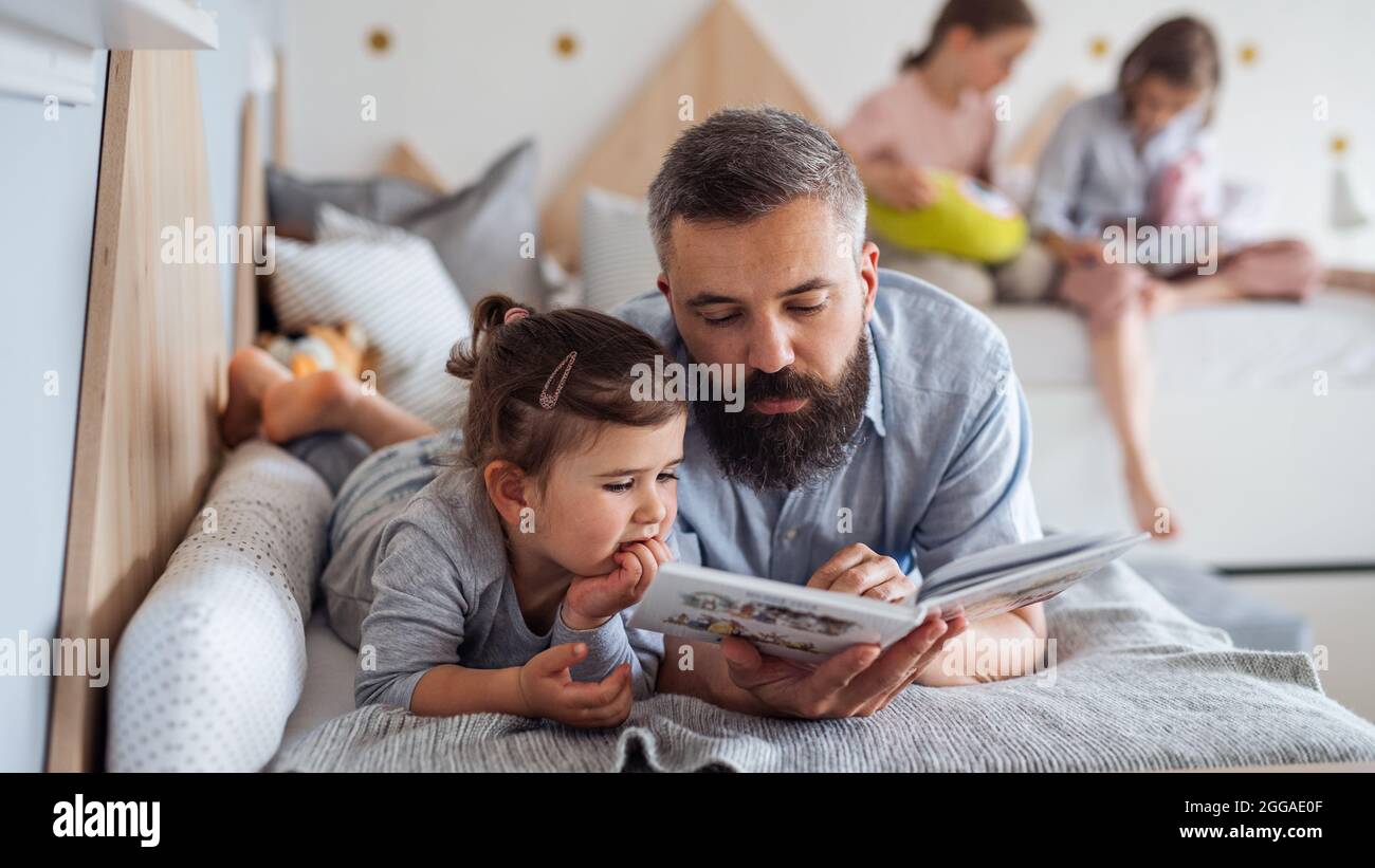 Père avec trois filles à l'intérieur à la maison, lisant un livre. Banque D'Images