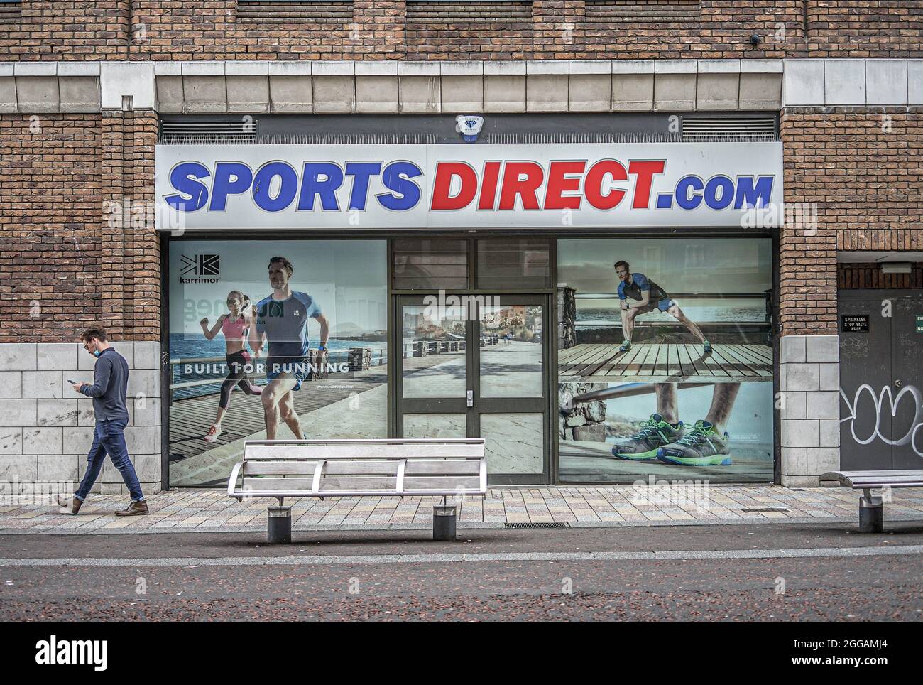 Belfast, Royaume-Uni. 22 août 2021. Un homme utilisant un téléphone portable passe devant le magasin Sports Direct.com Sportswear, dans Lombard Street. Crédit : SOPA Images Limited/Alamy Live News Banque D'Images