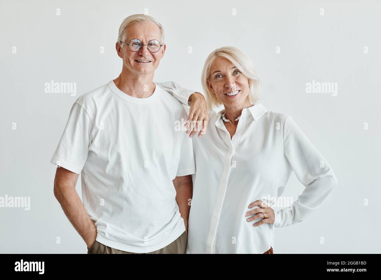 Portrait minimal de couple senior moderne, vêtu de blanc sur fond blanc et souriant à l'appareil photo Banque D'Images