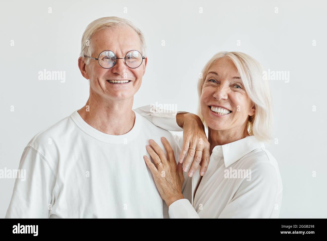 Portrait minimal d'un couple senior moderne portant du blanc sur fond blanc et souriant à l'appareil photo Banque D'Images