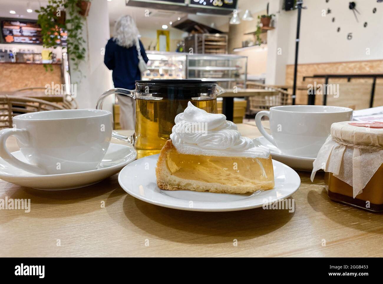 Gros plan d'un morceau de gâteau transparent en gélatine avec crème de meringue sur la table dans un café avec visiteur flou. Banque D'Images Gros plan d'un morceau de gâteau transparent en gélatine avec crème de meringue sur la table dans un café avec visiteur flou. Banque D'Images