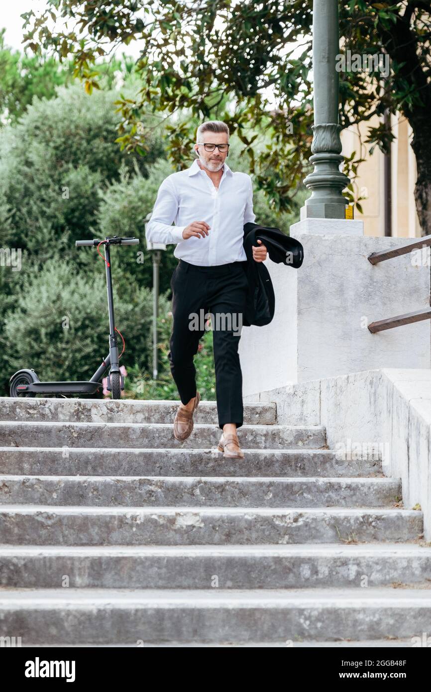 Homme d'affaires descendant les escaliers pour prendre son train à la gare. Un jeune directeur financier s'est lancé dans les escaliers en parlant avec des écouteurs Banque D'Images