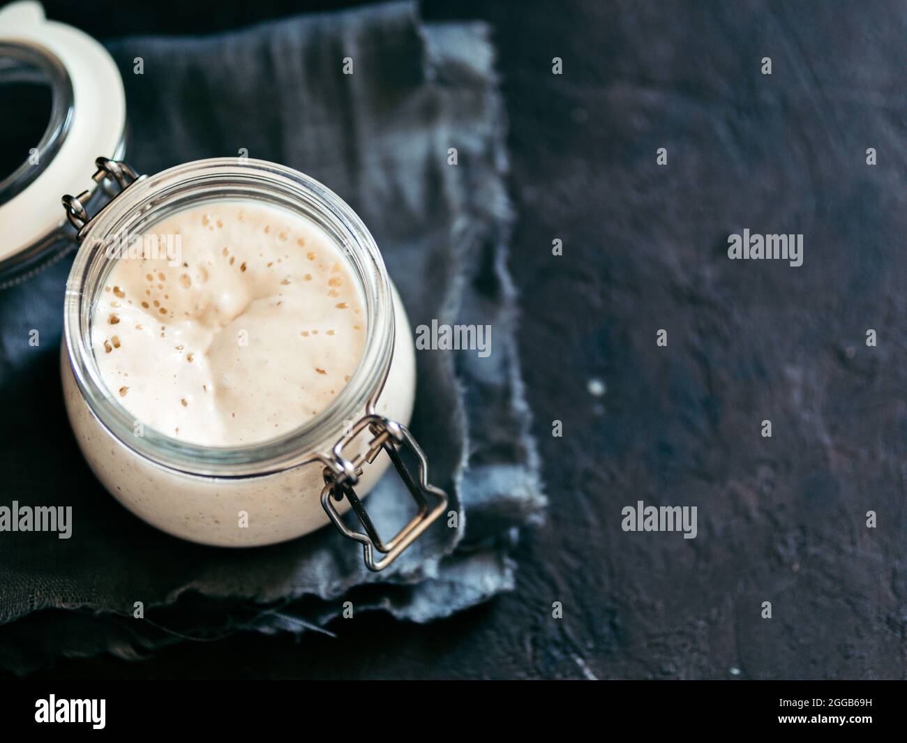 Démarreur de levain de blé. Bol en verre avec entrée de levain sur fond sombre, espace de copie. Banque D'Images