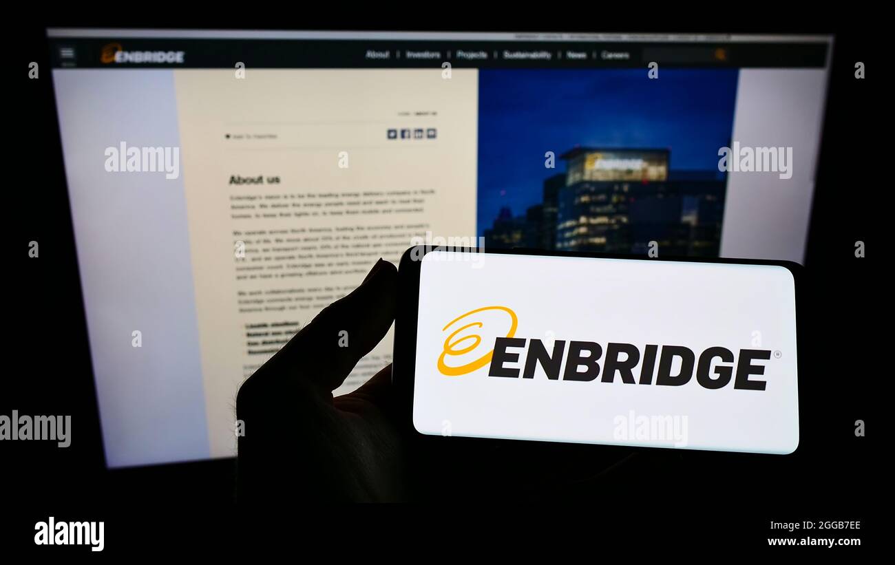 Personne qui tient un téléphone portable avec le logo de la société canadienne de pipeline Enbridge Inc. À l'écran devant la page Web des affaires. Mise au point sur l'affichage du téléphone. Banque D'Images