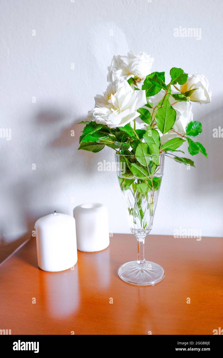Roses blanches dans un vase, bougies blanches sur une commode en bois sur un mur blanc.Design intérieur.Décoration d'intérieur. Banque D'Images Roses blanches dans un vase, bougies blanches sur une commode en bois sur un mur blanc.Design intérieur.Décoration d'intérieur. Banque D'Images
