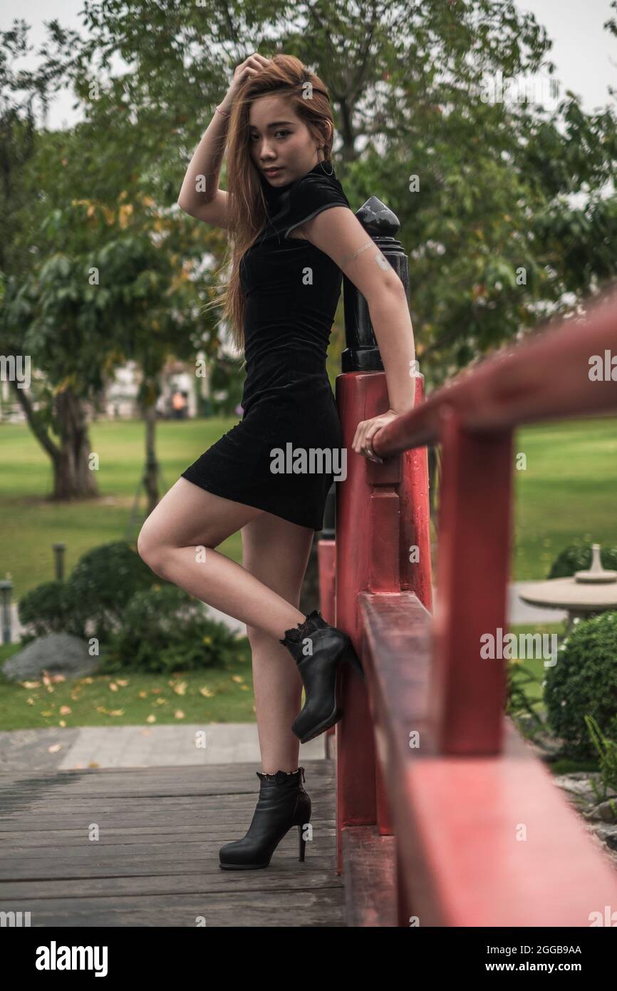 Belle jeune femme asiatique en robe noire mini debout près de la main courante dans le parc. Penché sur la main courante. Jolie fille vietnamienne. Haute qualité Banque D'Images