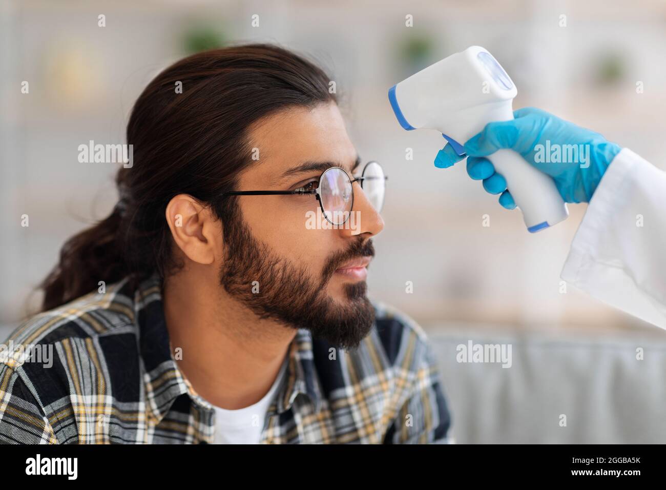 Médecin méconnaissable en costume de protection mesurant la température corporelle pour l'homme Banque D'Images