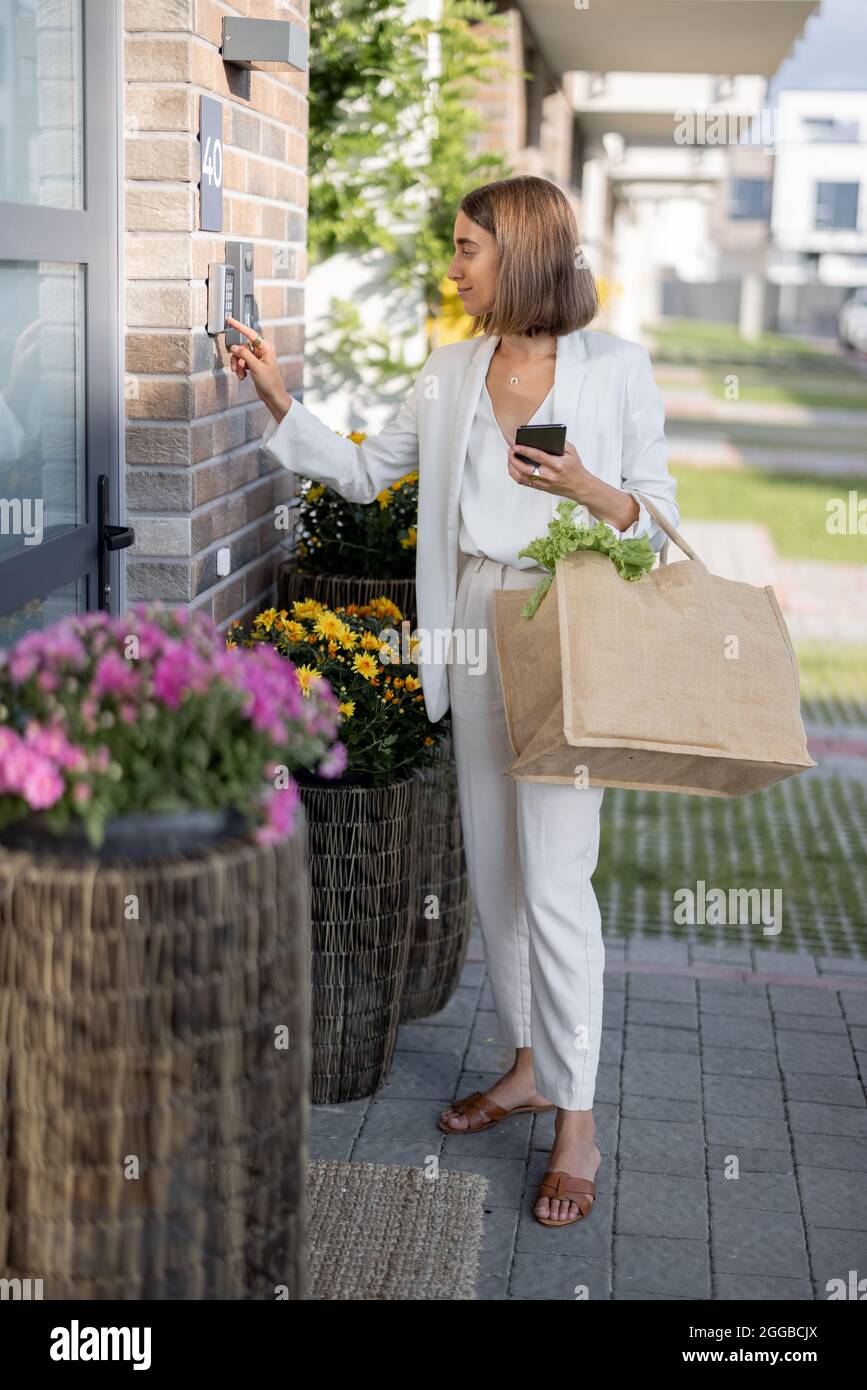 Une femme rentre chez elle avec des articles d'épicerie et entre un code pour accéder à la porte Banque D'Images