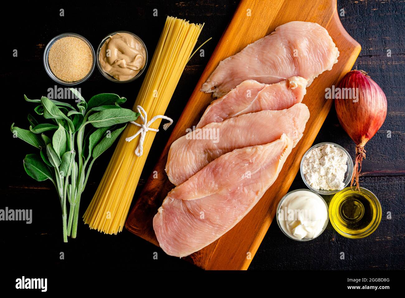 Poulet crémeux à la moutarde et aux pâtes à l'ange Ingrédients : côtelettes de poulet, capellini, sauge fraîche et autres ingrédients sur une table en bois sombre Banque D'Images
