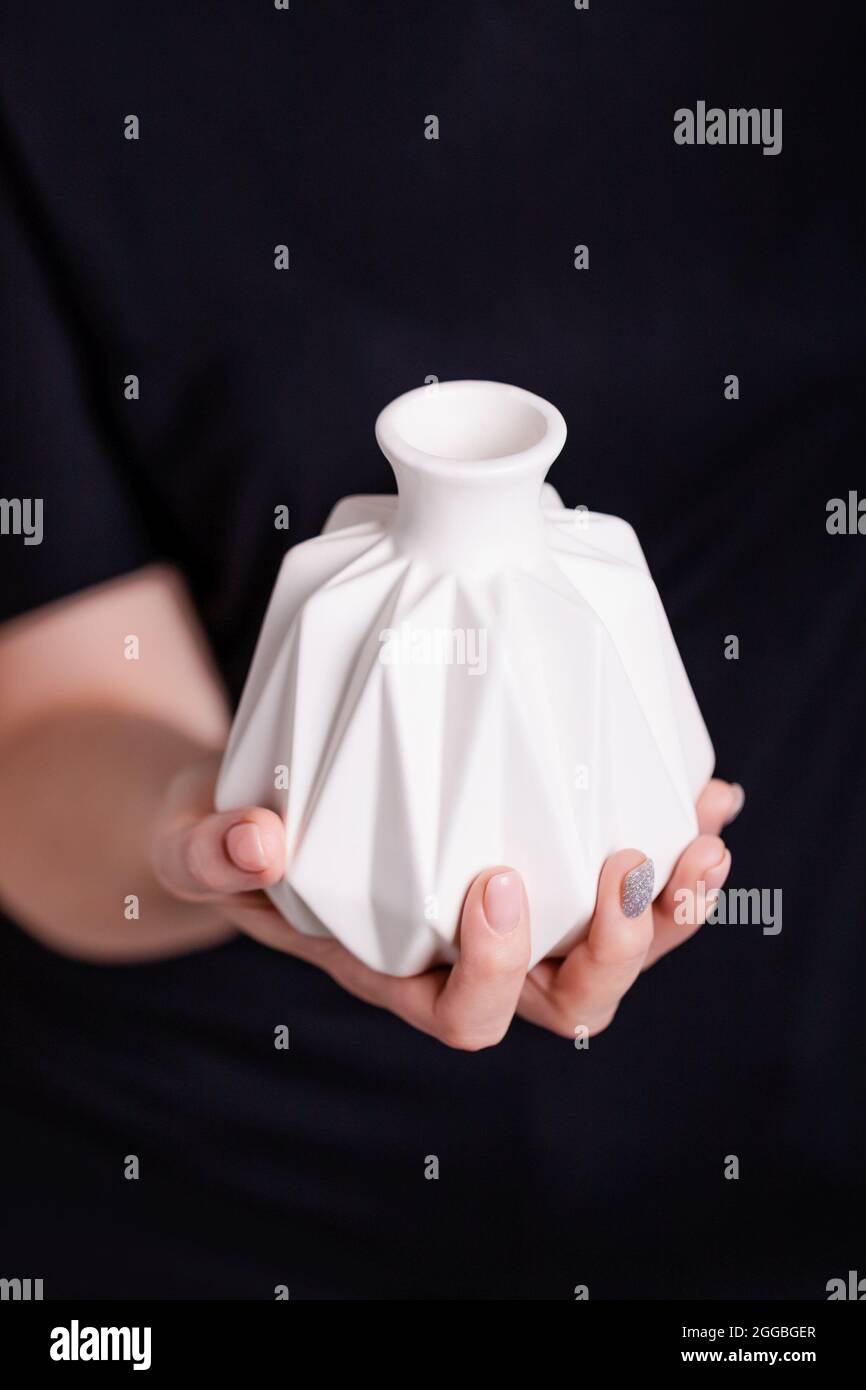 Belle main femelle tenant un vase en céramique blanc sur fond noir. Manucure avec vernis à ongles rose et gris Banque D'Images