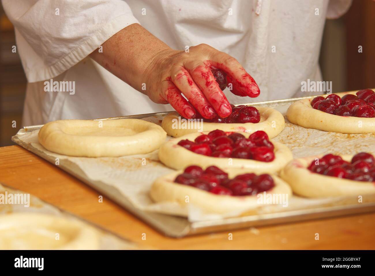 La femme sur la photo fait des tartes aux fruits. Les mains remplissent la pâte à tarte avec des fraises. Travail dans la boulangerie. Banque D'Images