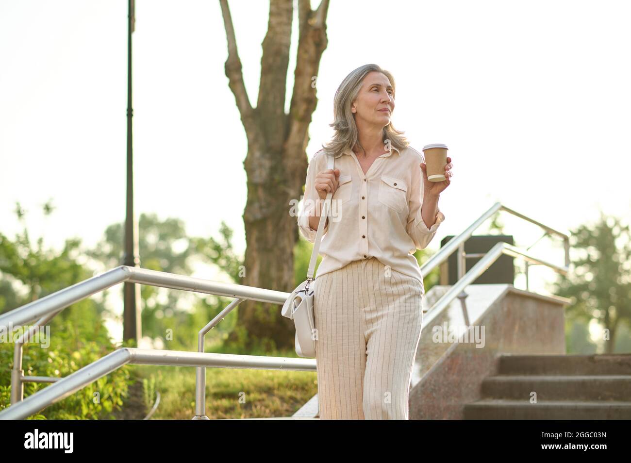 Femme pensive avec café dans les escaliers dans le parc Banque D'Images