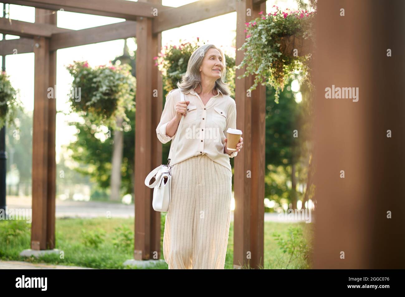 Femme avec café regardant des fleurs dans le parc Banque D'Images