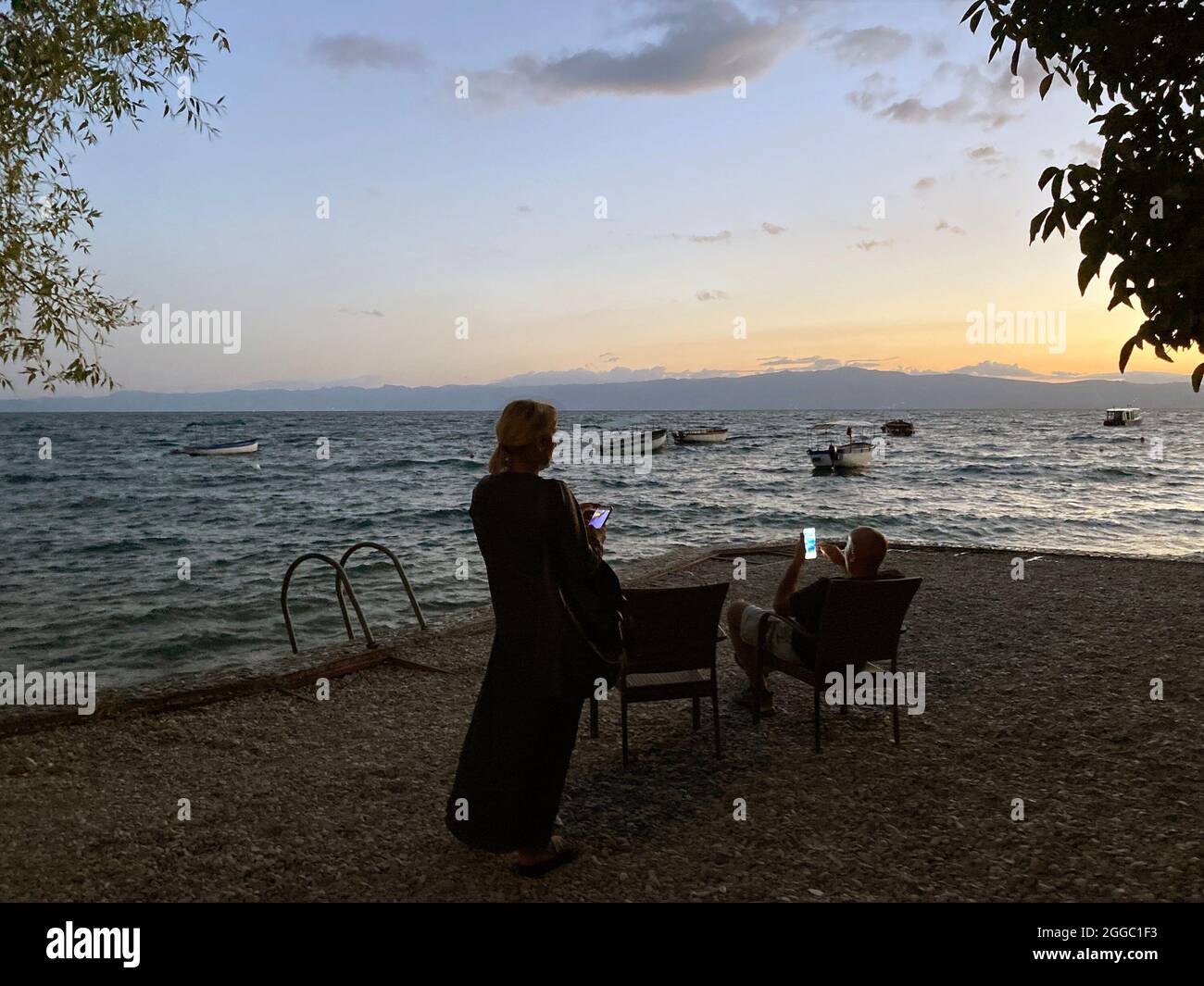 homme et femme regardent leurs smartphones en arrière-plan du lac et du coucher du soleil Banque D'Images