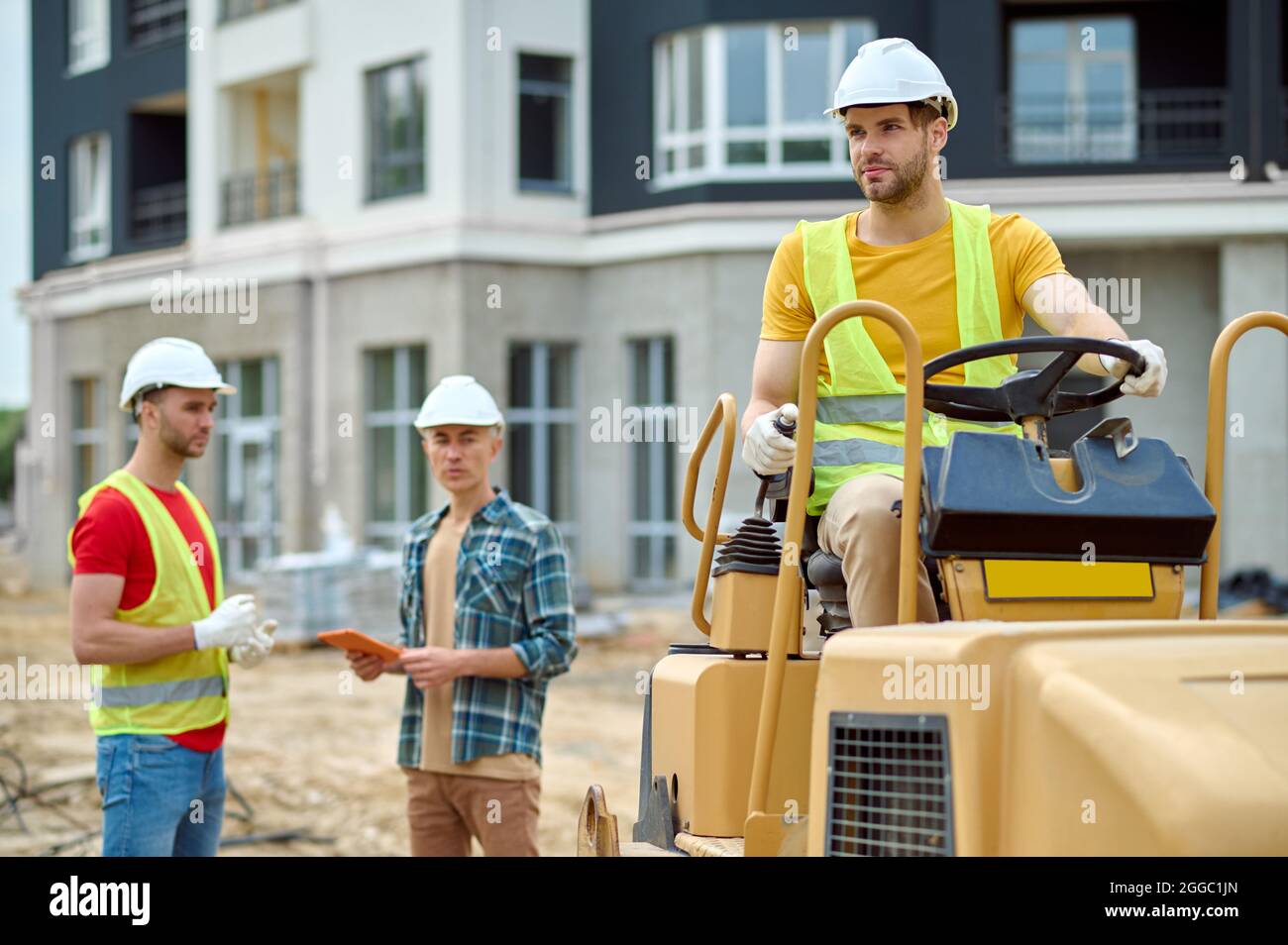 Trois ouvriers de construction qualifiés et attirants dans des casques de chantier sur le chantier Banque D'Images